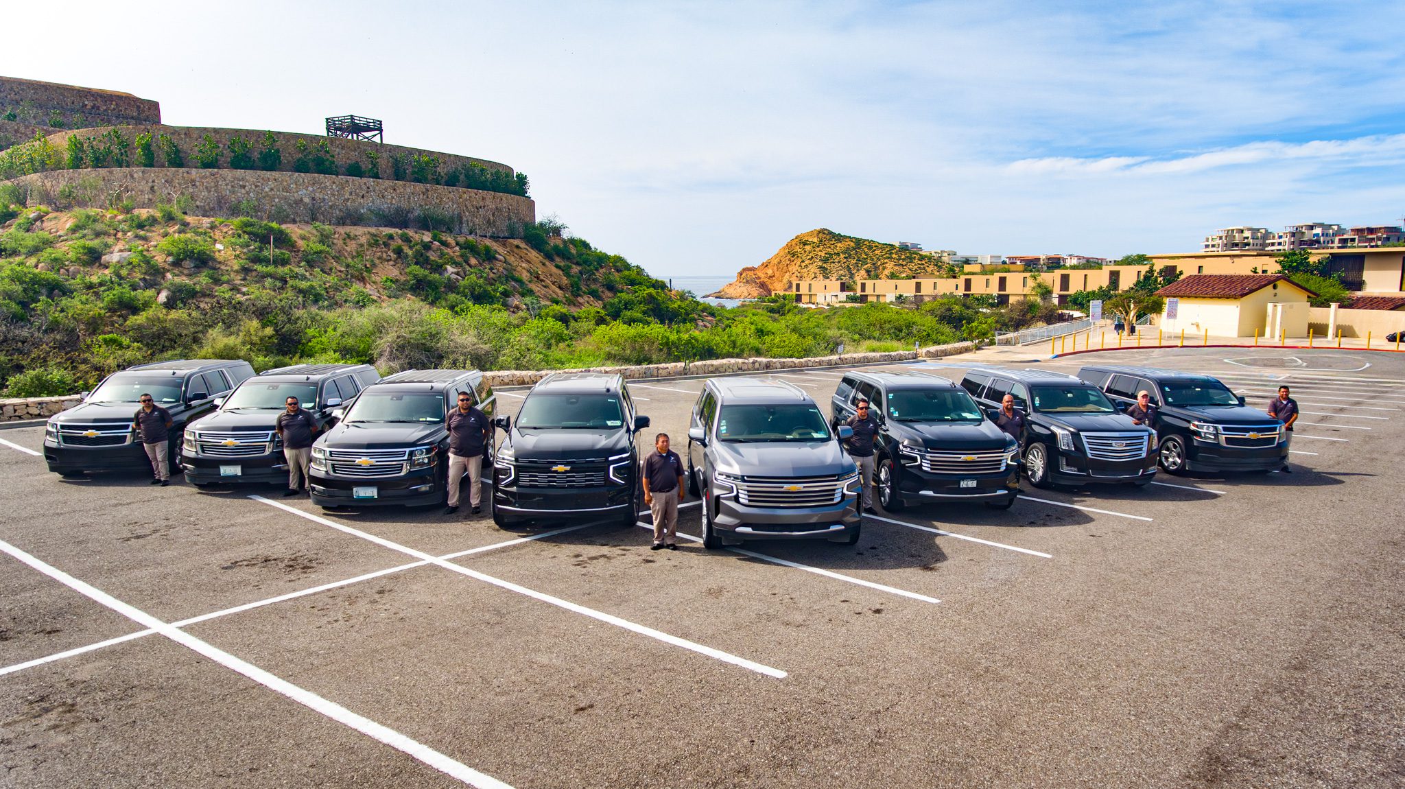 Cabo Airport Shuttles driver team standing beside the SUV fleet overlooking the Los Cabos coastline